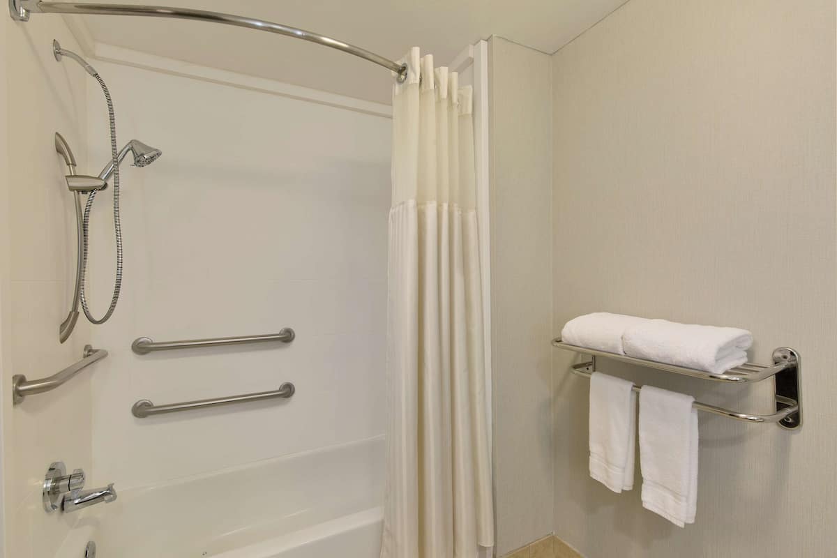 A bathroom with a shower, grab bars, a towel rack, and a curtain.