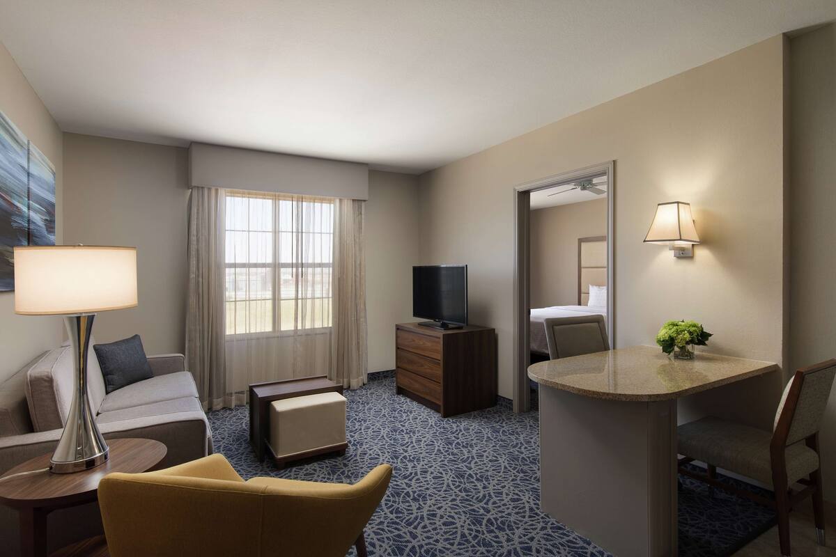 A hotel room with a bed, a desk, a chair, a TV, a lamp, and a window with curtains.