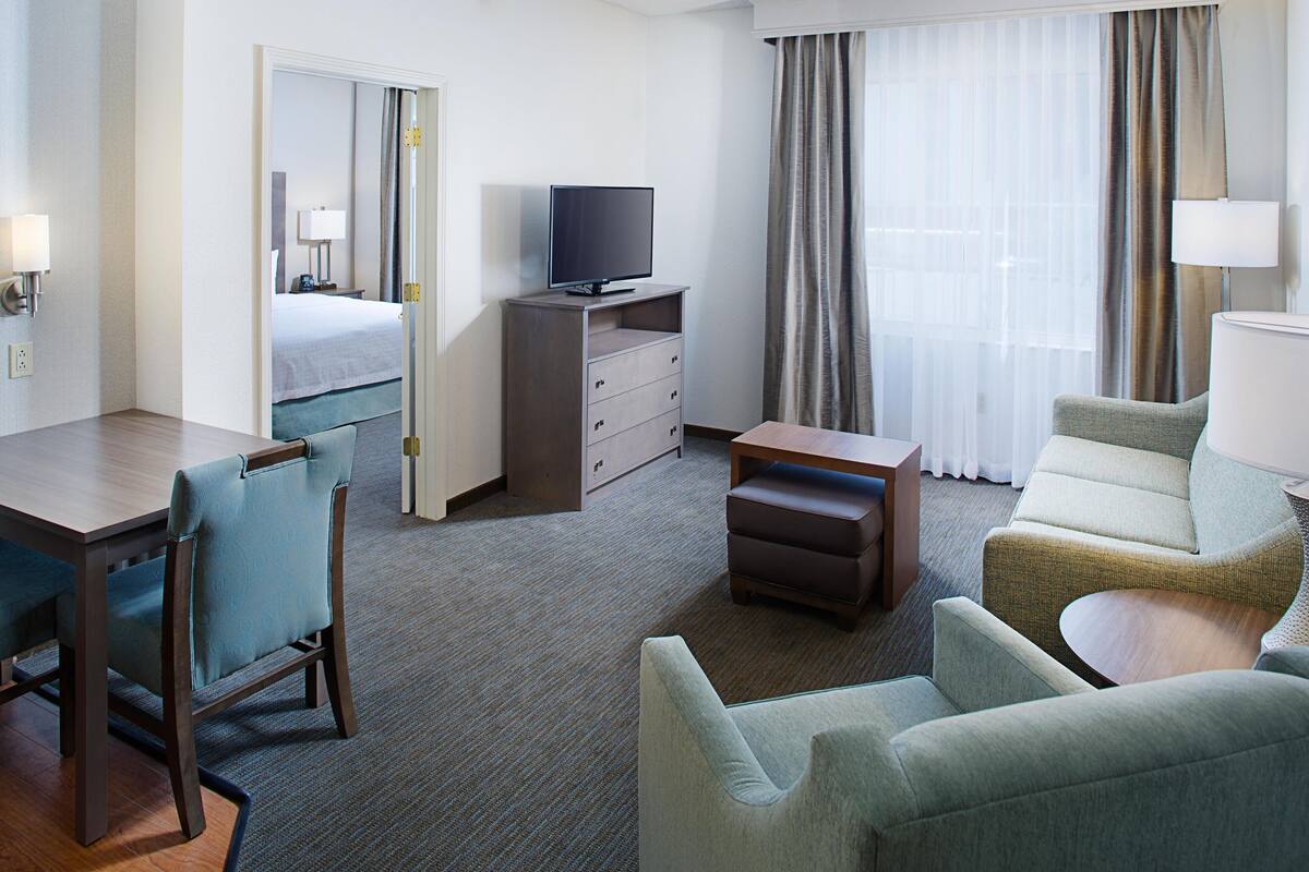A hotel room with a bed, a television on a stand, a desk with a chair, and a sofa.