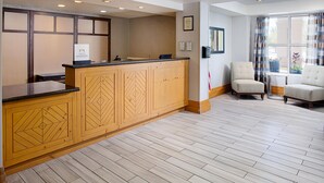 A hotel reception area with a wooden reception desk, a seating area with two chairs, and a large window with curtains. - Homewood Suites by Hilton Albuquerque Uptown (Albuquerque)