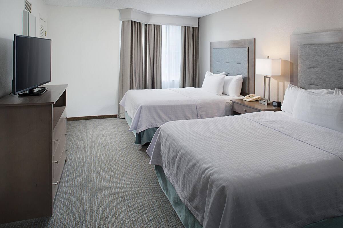 A hotel room with two beds, a television, a desk with a lamp, and a telephone.