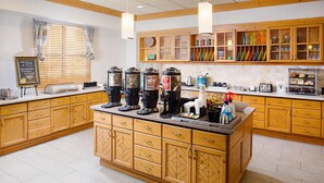 A kitchen with wooden cabinets, a central island with coffee machines, and a breakfast bar. - Homewood Suites by Hilton Albuquerque Uptown (Albuquerque)