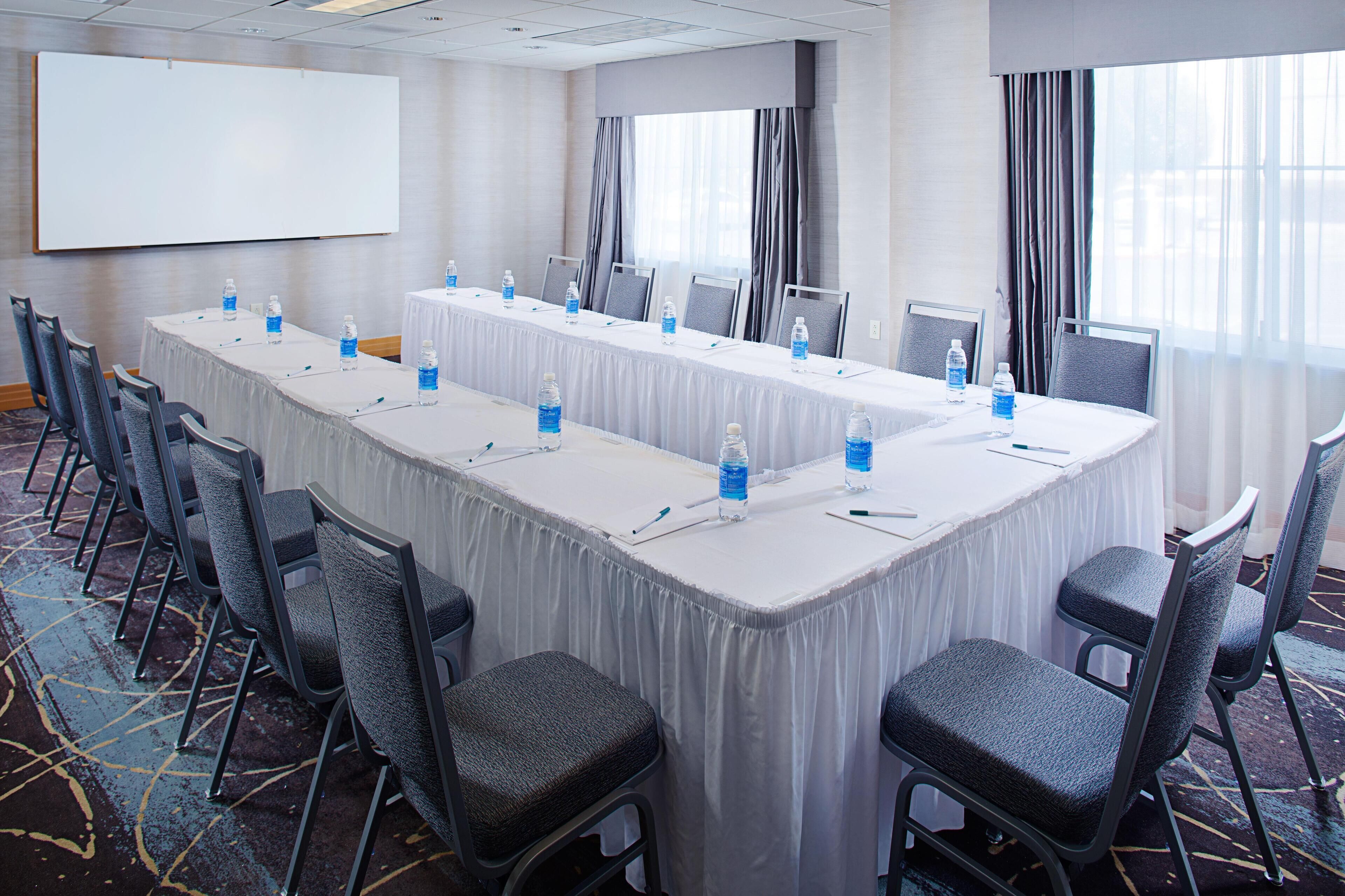 A conference room with a long table, chairs, a projector screen, and windows with curtains.