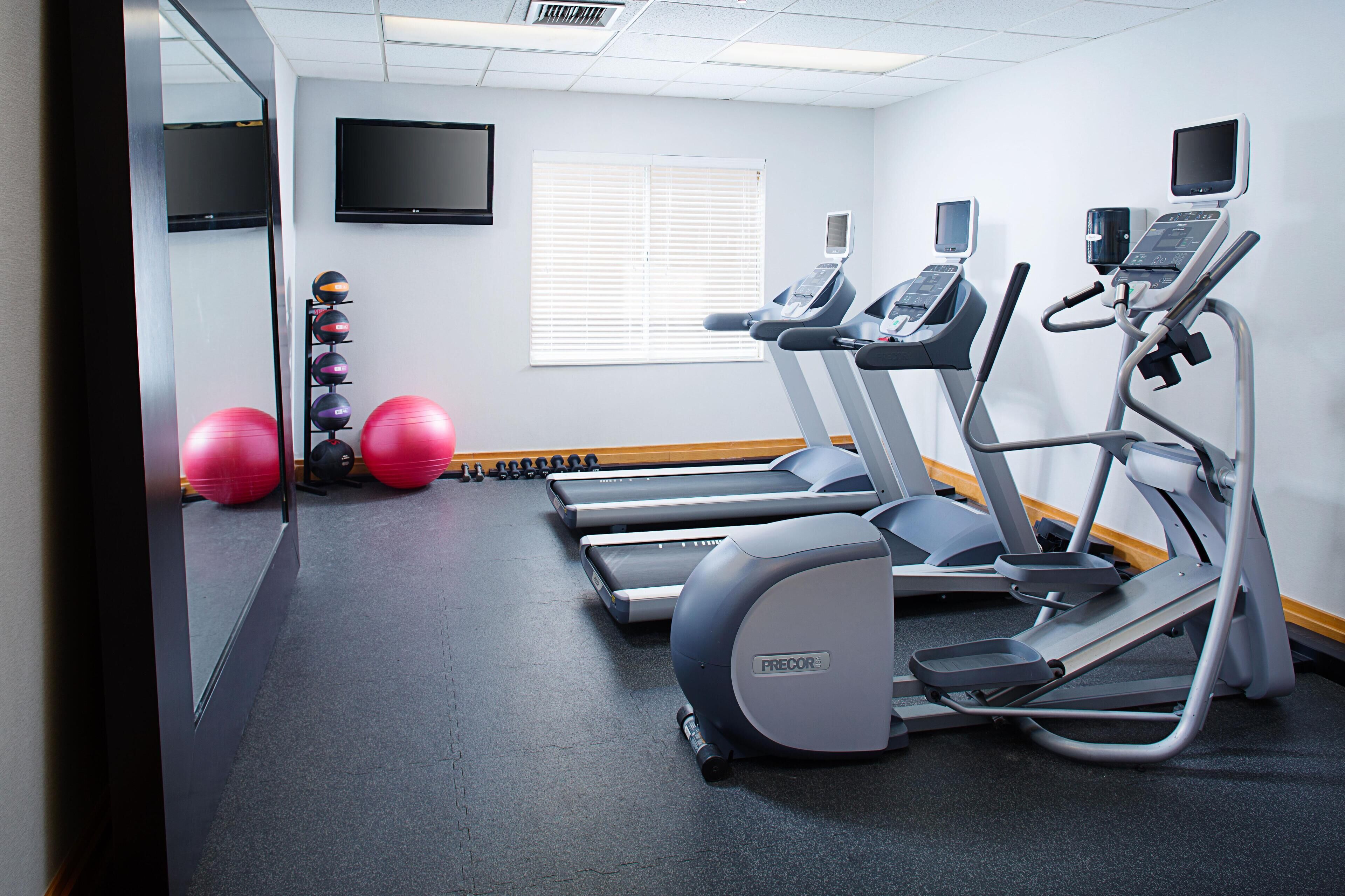 A gym with treadmills, exercise balls, and a TV screen on the wall.
