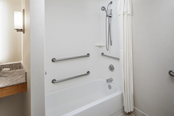 A bathroom with a white bathtub, grab bars, a showerhead, and a towel rack.