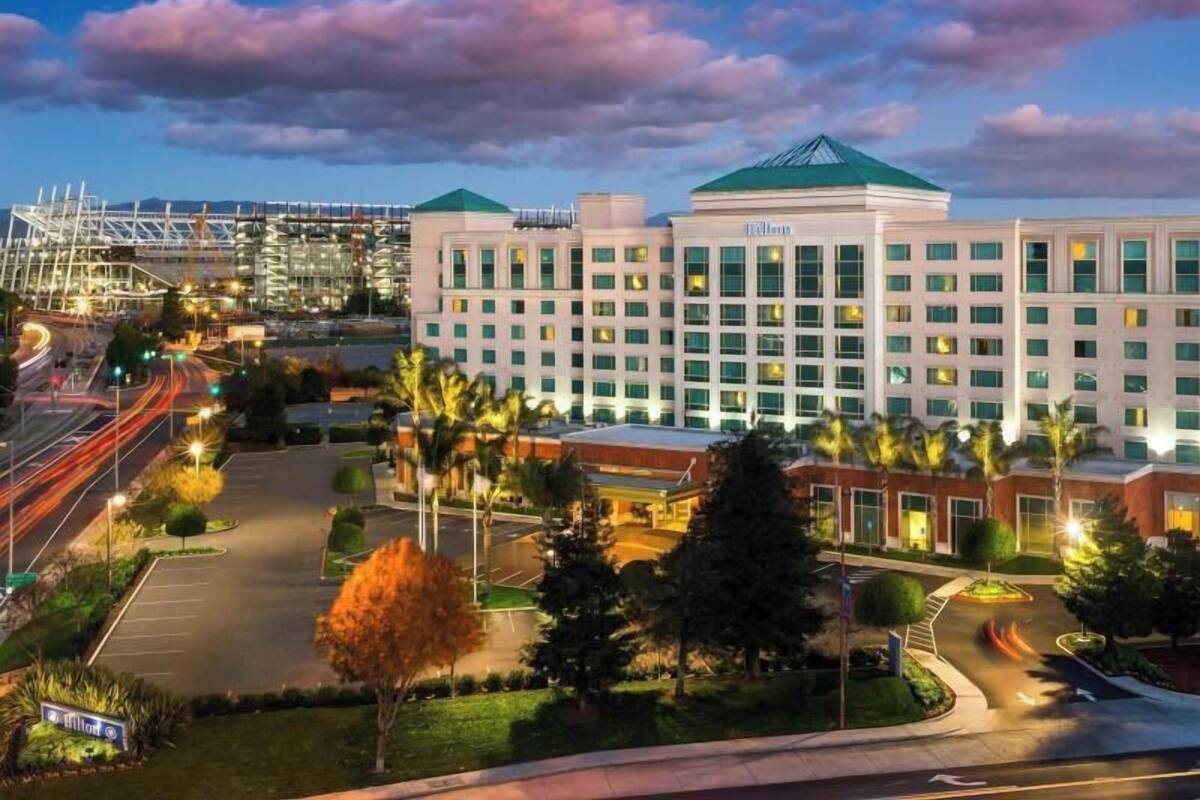 A hotel with a central building, a parking lot, and surrounding greenery.