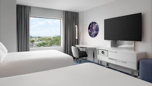 Una habitación de hotel moderna con una cama grande, un escritorio, una silla, un televisor de pantalla plana y vistas a la ciudad.
