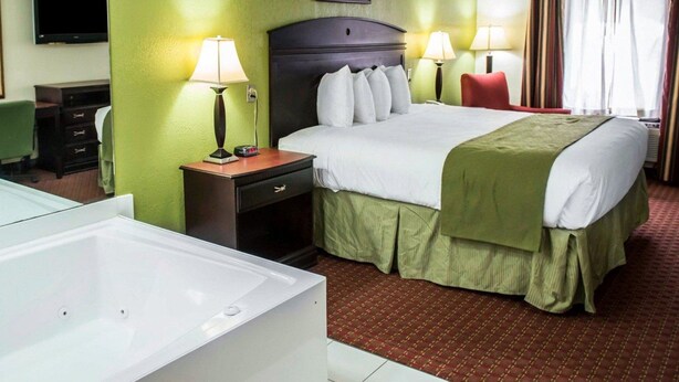 A hotel room with a large bed, two bedside lamps, a flat-screen TV, a desk with a chair, and a large white bathtub.