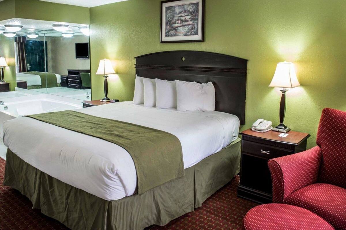 A hotel room with a large bed, a mirror, two bedside lamps, a telephone, and a red chair.