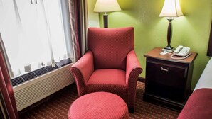 A hotel room with a red polka dot armchair, a matching ottoman, a bedside table with a lamp, and a phone.