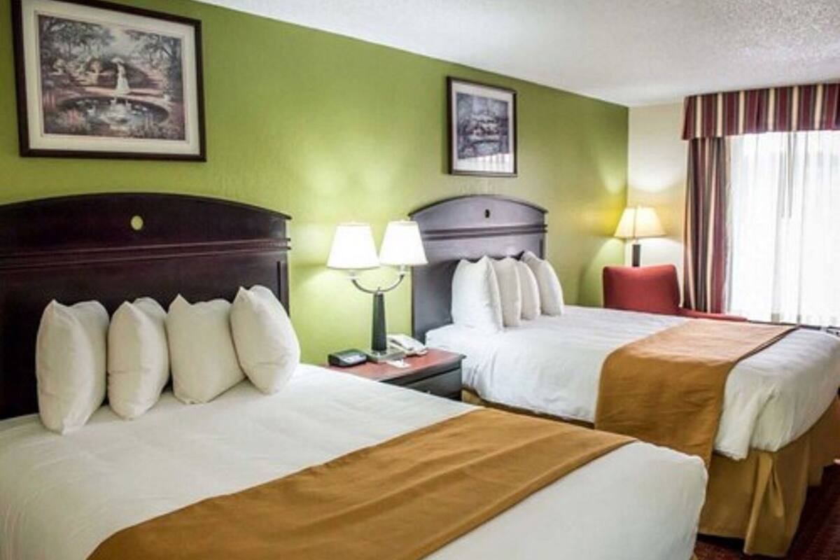 A hotel room with two beds, green walls, framed pictures, and a window with curtains.