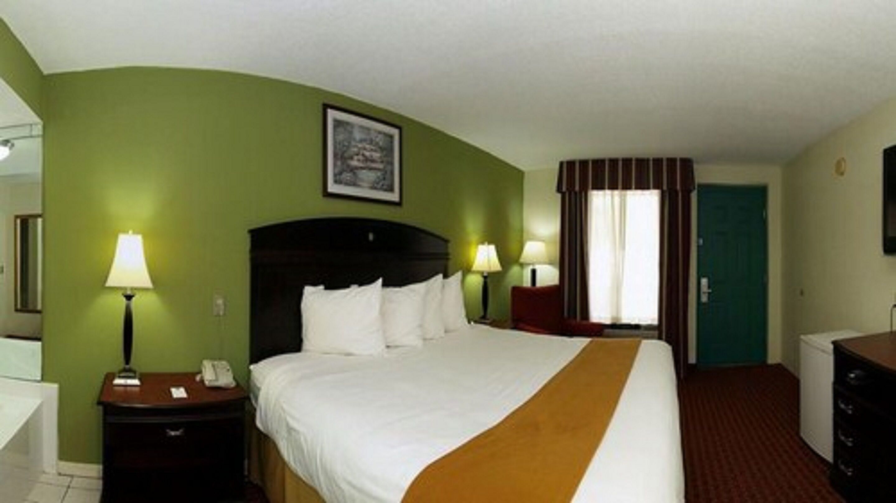 A hotel room with a bed, two bedside lamps, a nightstand, a dresser, a door, and a framed picture on the wall.
