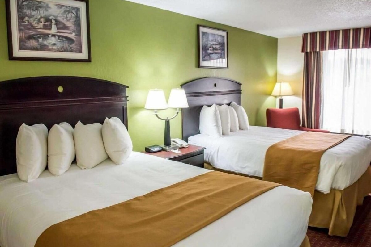 A hotel room with two beds, green walls, framed pictures, a red chair, and a window with curtains.