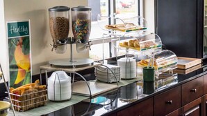 A breakfast bar with cereal dispensers, a fruit basket, and a sign labeled "Healthy".
