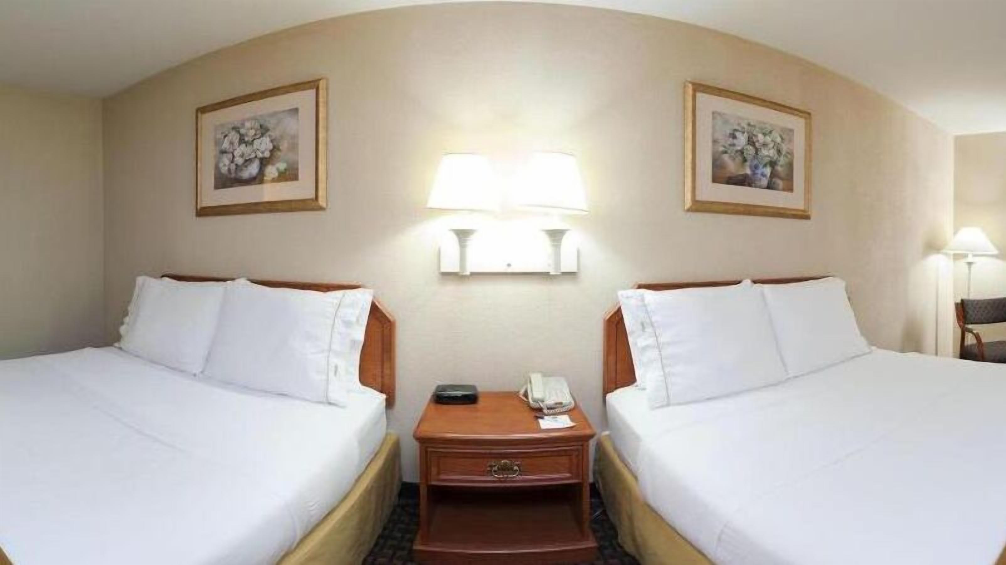Une chambre d’hôtel avec deux lits, une table de chevet avec une lampe et deux tableaux encadrés accrochés aux murs.
