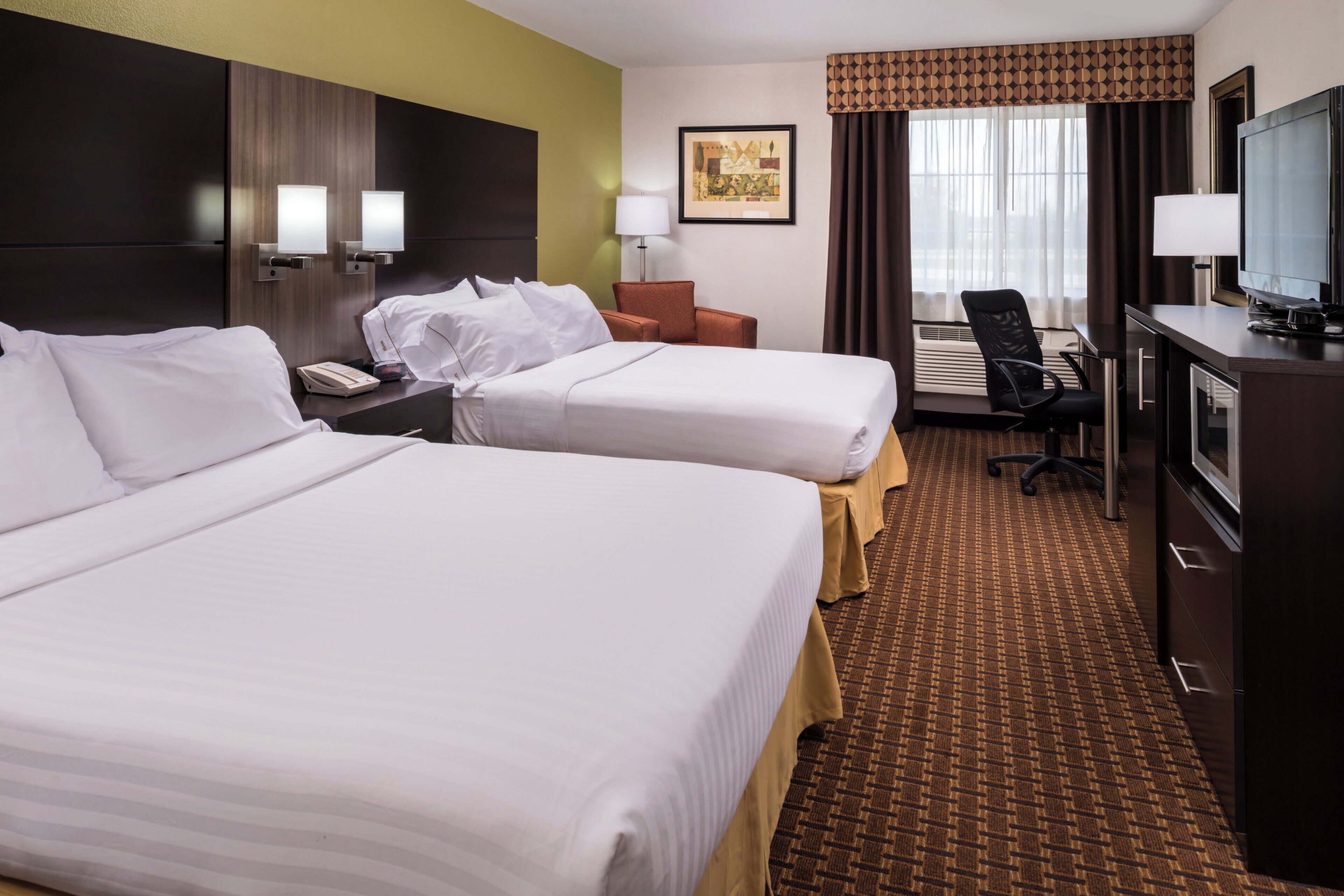 A hotel room with two beds, a desk, a chair, a television, and a window with curtains.