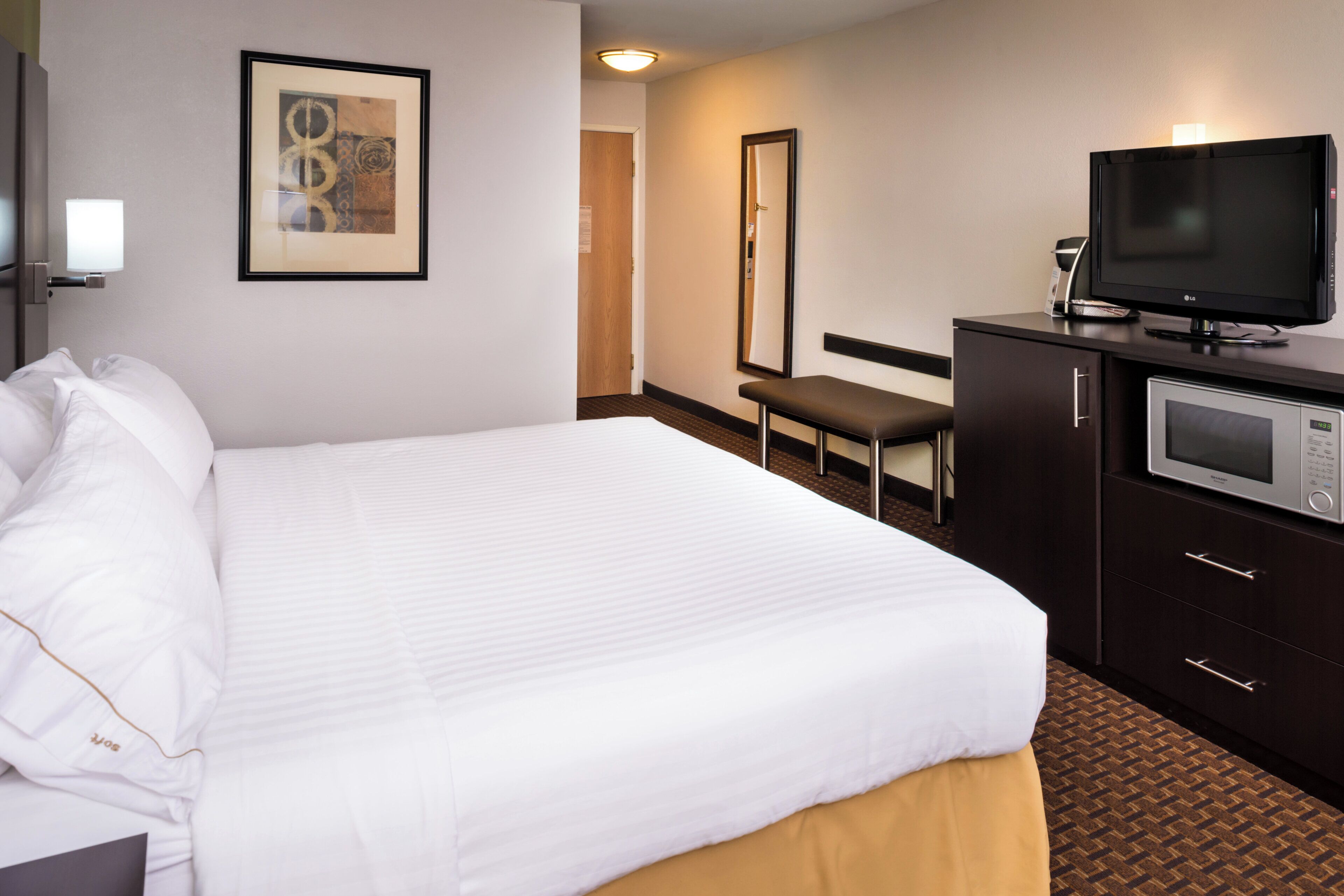 A hotel room with a large bed, a television, a minibar, and a framed picture on the wall.