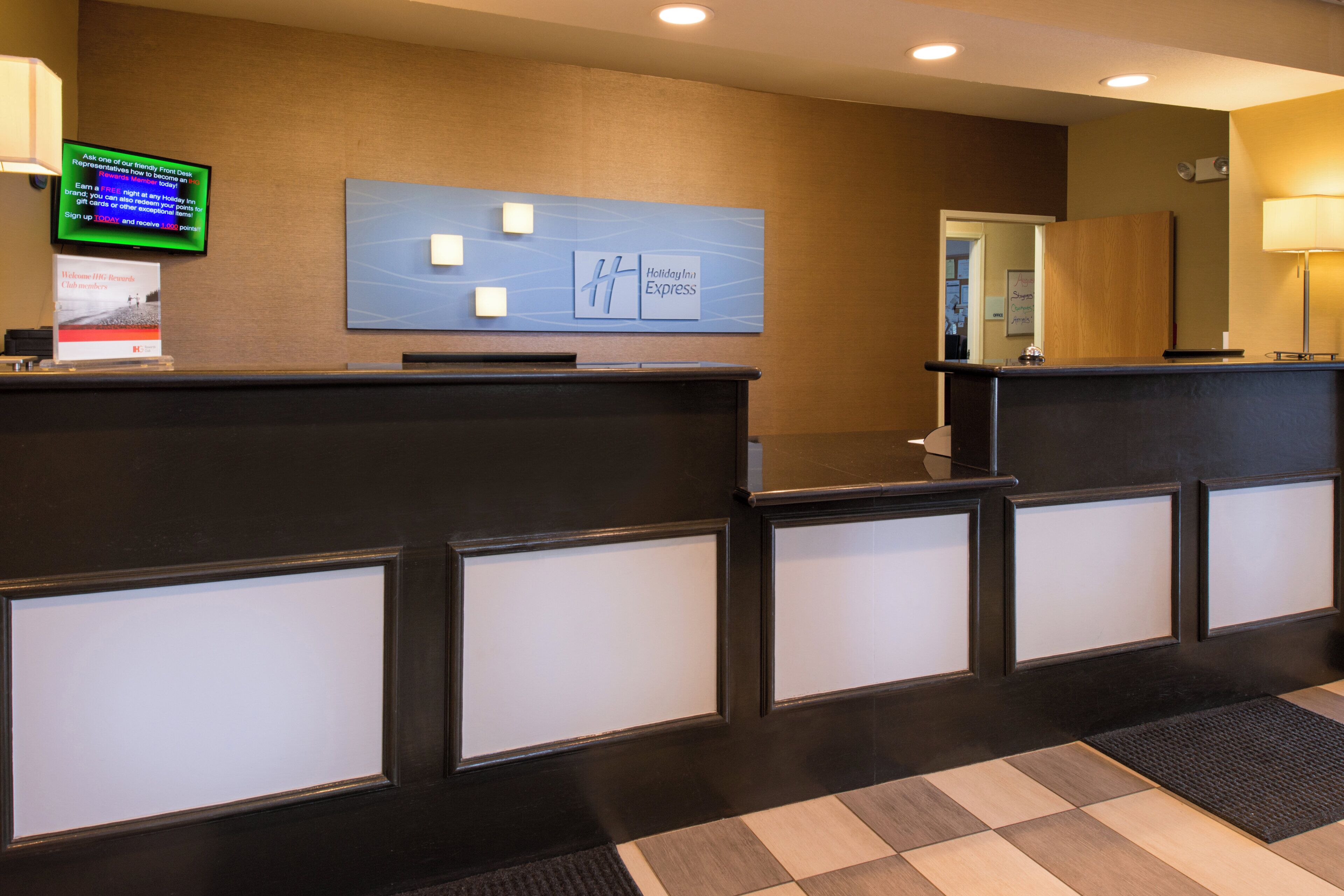 A hotel reception desk with a digital screen displaying information, a Holiday Inn Express sign, and a reception area with a check-in counter.