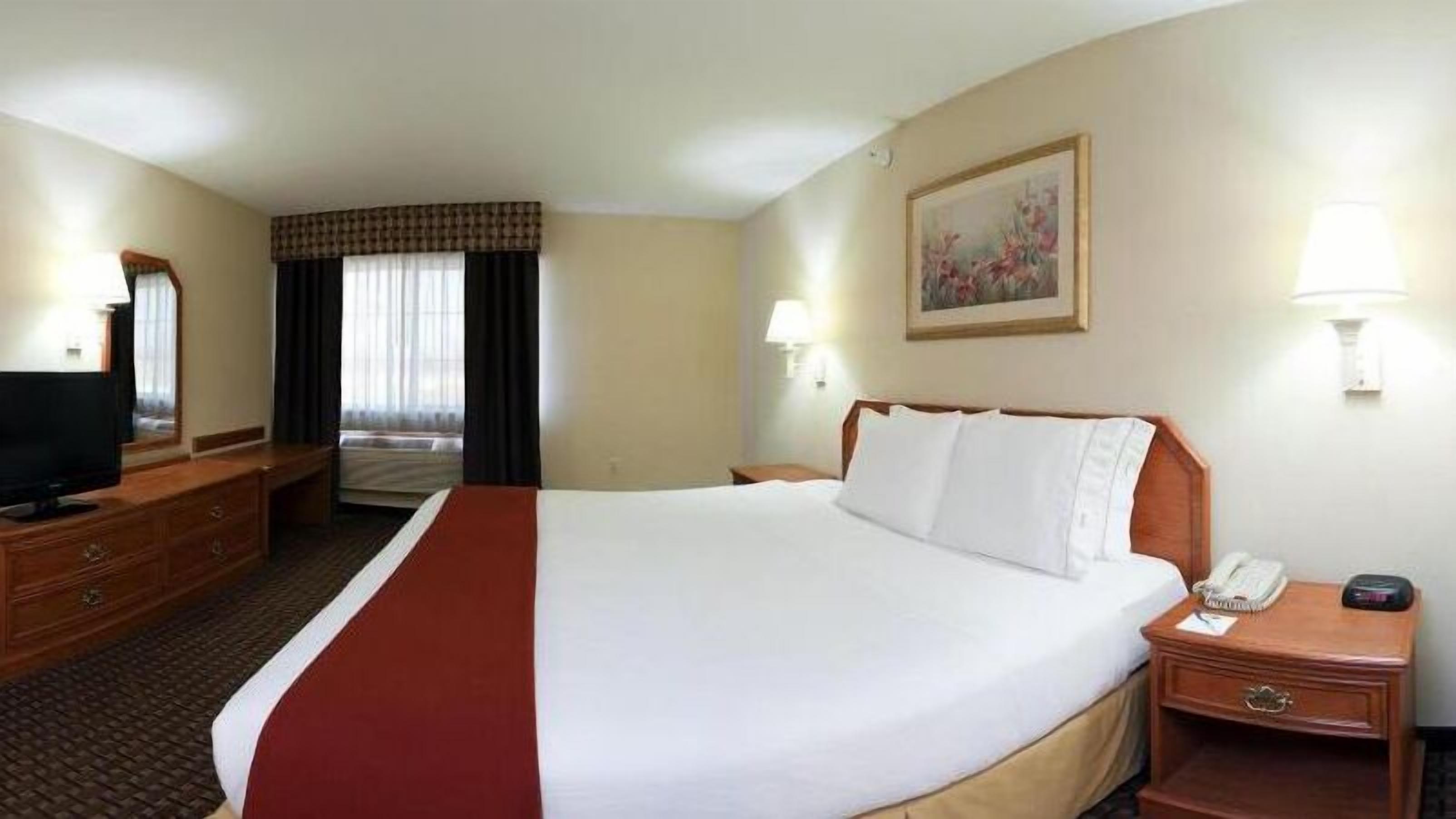 Quarto de hotel com uma cama grande, uma televisão, uma escrivaninha e um quadro na parede.