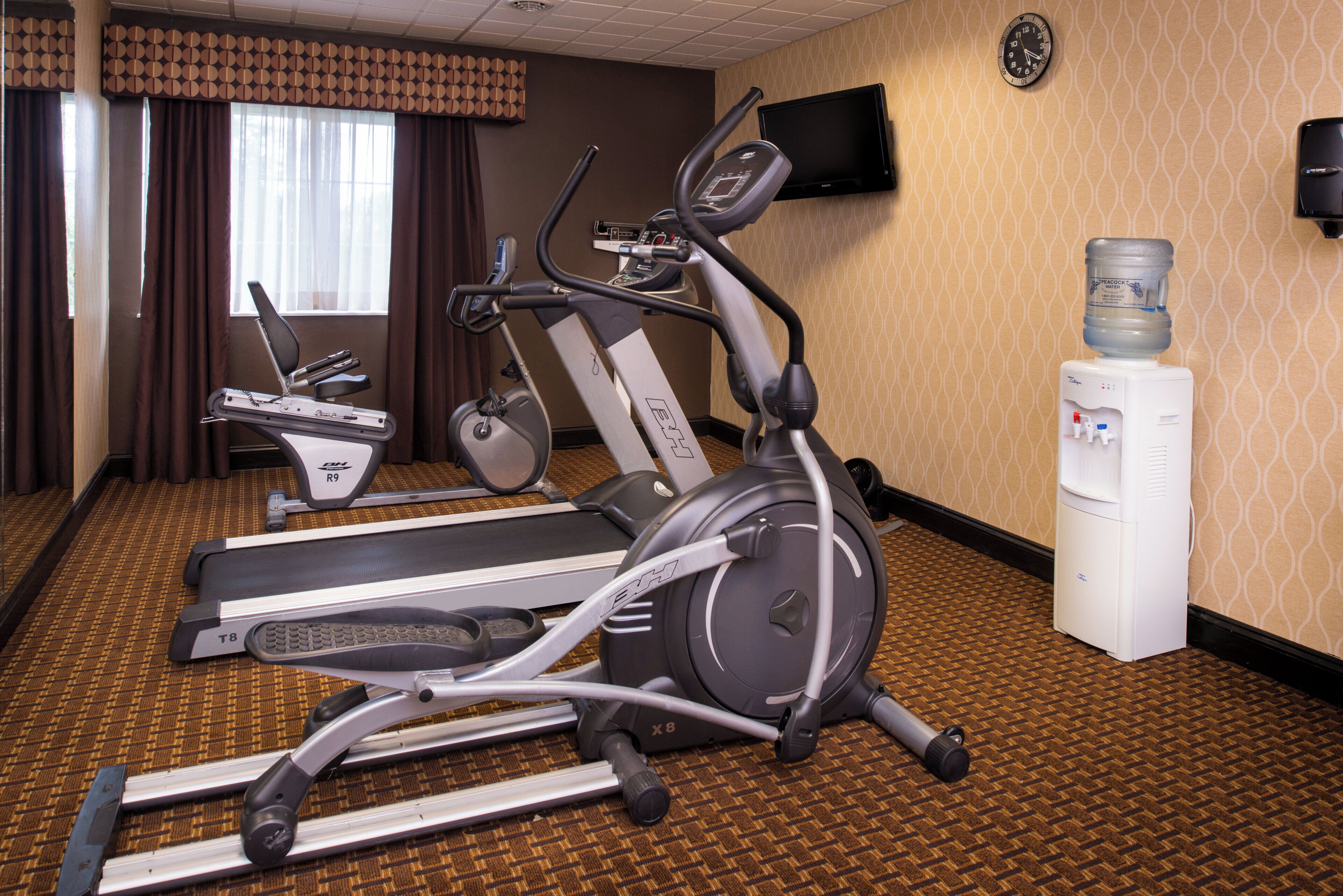 Habitación de hotel con equipo de ejercicio, que incluye una caminadora, una elíptica y una bicicleta estática.