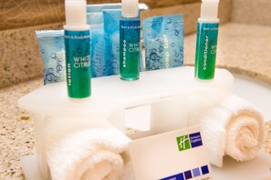 Artigos de higiene pessoal como shampoo, condicionador e sabonetes em barra sobre uma bandeja branca com uma toalha.