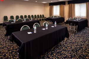 Un salón de conferencias con mesas, sillas, botellas de agua y una alfombra estampada.