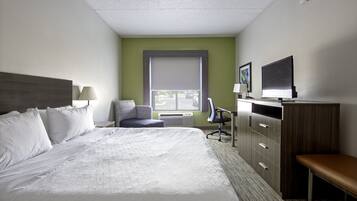 Quarto de hotel com uma cama grande, uma escrivaninha, uma cadeira, uma televisão e uma janela com persianas.