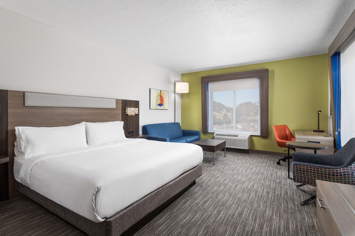 Ein Hotelzimmer mit einem großen Bett, einem blauen Sofa, einem kleinen Tisch und einem Fenster mit Blick auf die Berge.