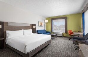 A hotel room with a large bed, a blue sofa, a small table, and a window with a mountain view.