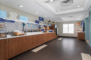 A modern breakfast area with a bakery section, a counter with various food items, and a clean, tiled floor.