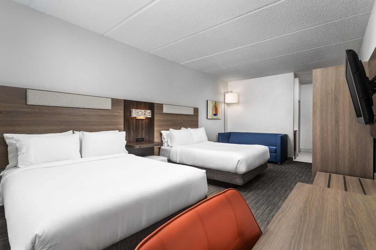 Ein Hotelzimmer mit zwei Betten, einem Schreibtisch, einem Stuhl, einem Fernseher und einem Wandbild.