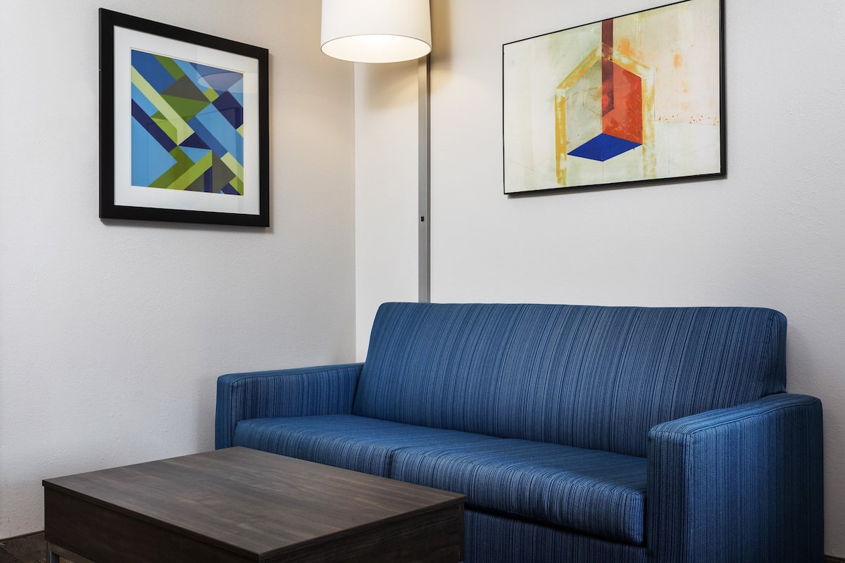 Ein Zimmer mit einem blauen Sofa, einem Holztisch und zwei gerahmten abstrakten Kunstwerken an der Wand.