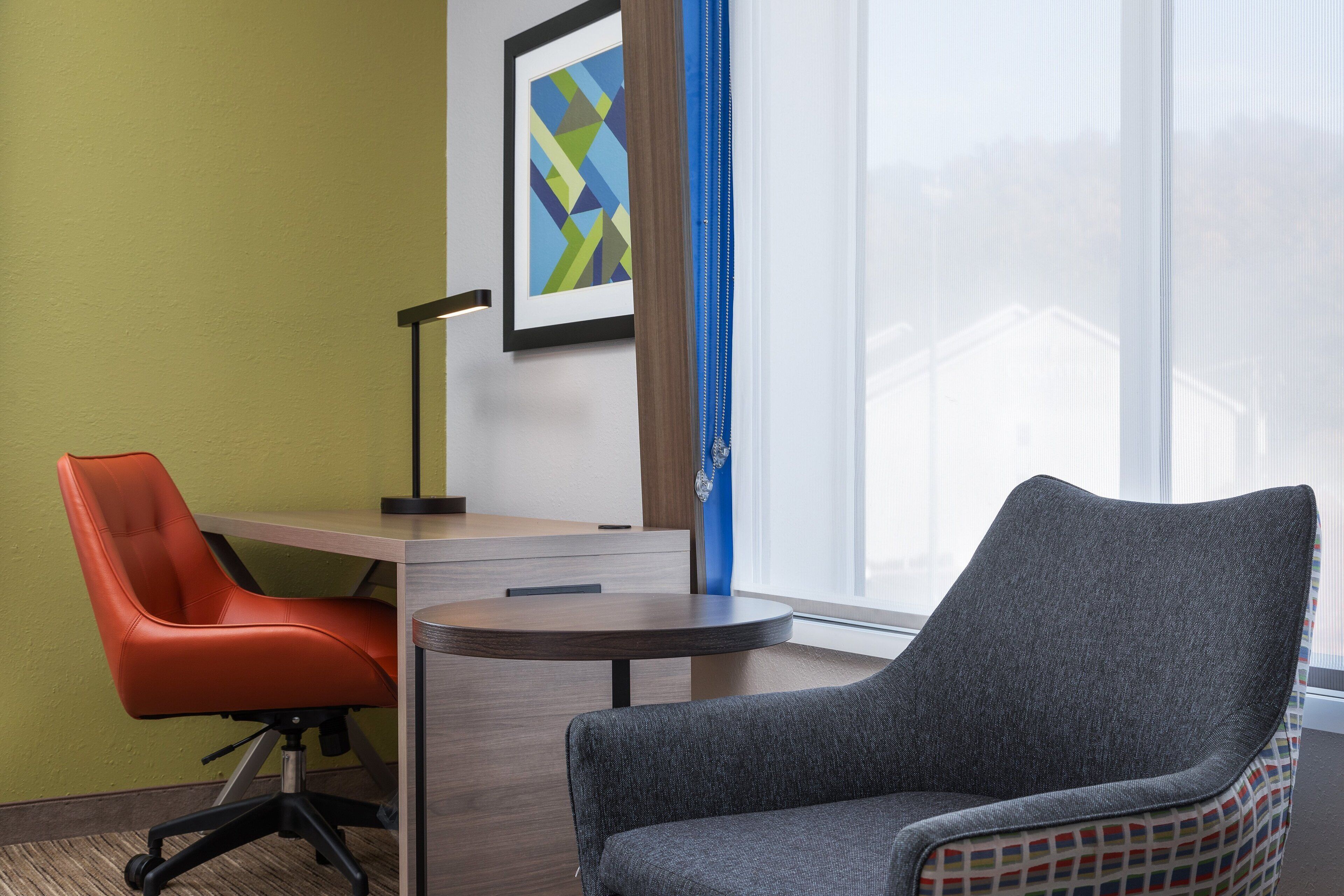 A modern office space with a desk, two chairs, a lamp, and a large window with curtains.