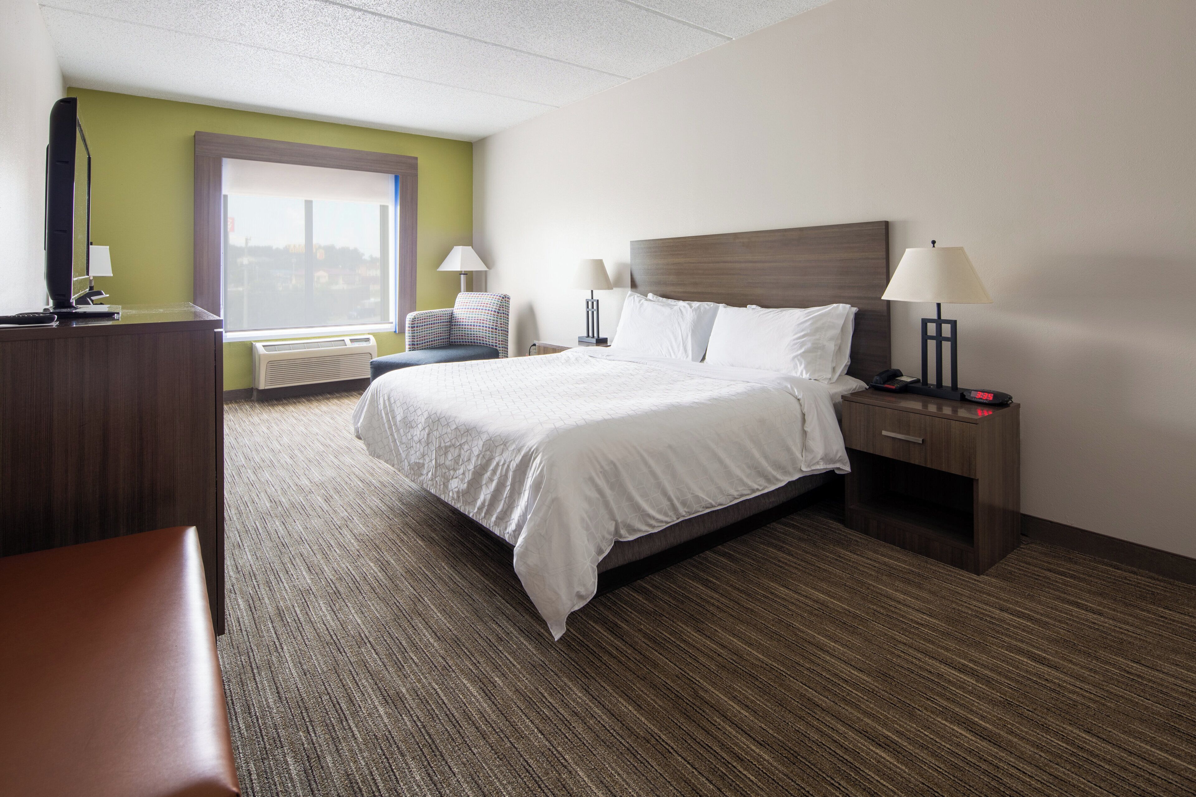 A hotel room with a bed, bedside tables, a desk, a chair, and a window.