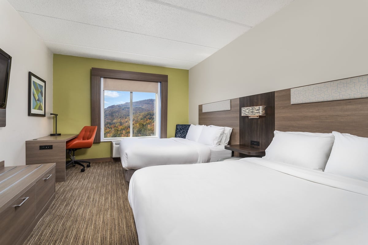Ein Hotelzimmer mit zwei Betten, einem Schreibtisch, einem Stuhl und einem Fenster mit Bergblick.