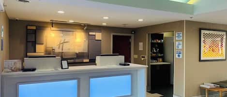 A hotel reception desk with a digital display, a check-in counter, and a wall-mounted sign indicating check-in and check-out times.