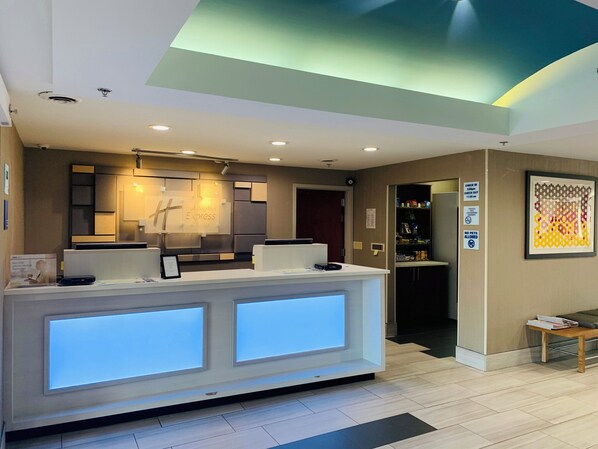 A hotel reception desk with a digital display, a check-in counter, and a wall-mounted sign indicating check-in and check-out times.