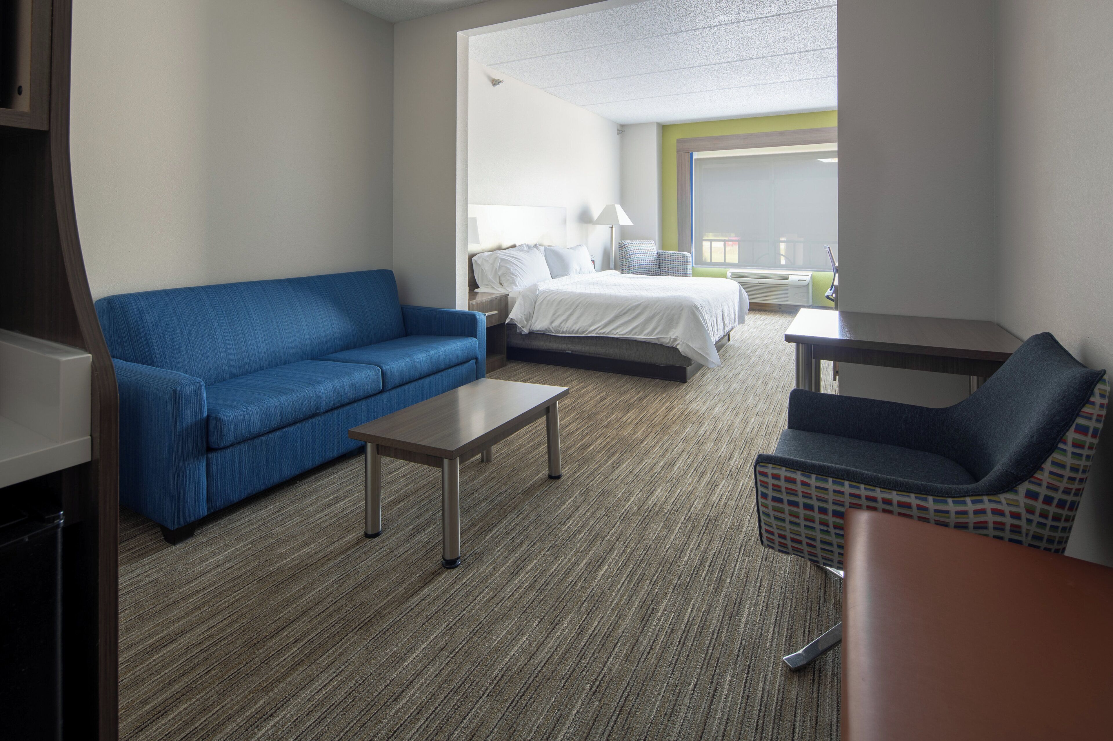 Habitación de hotel con sofá azul, cama con ropa blanca, una mesita y una silla estampada.