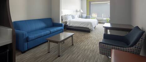 A hotel room with a blue sofa, a bed with white linens, a small table, and a chair with a colorful pattern.