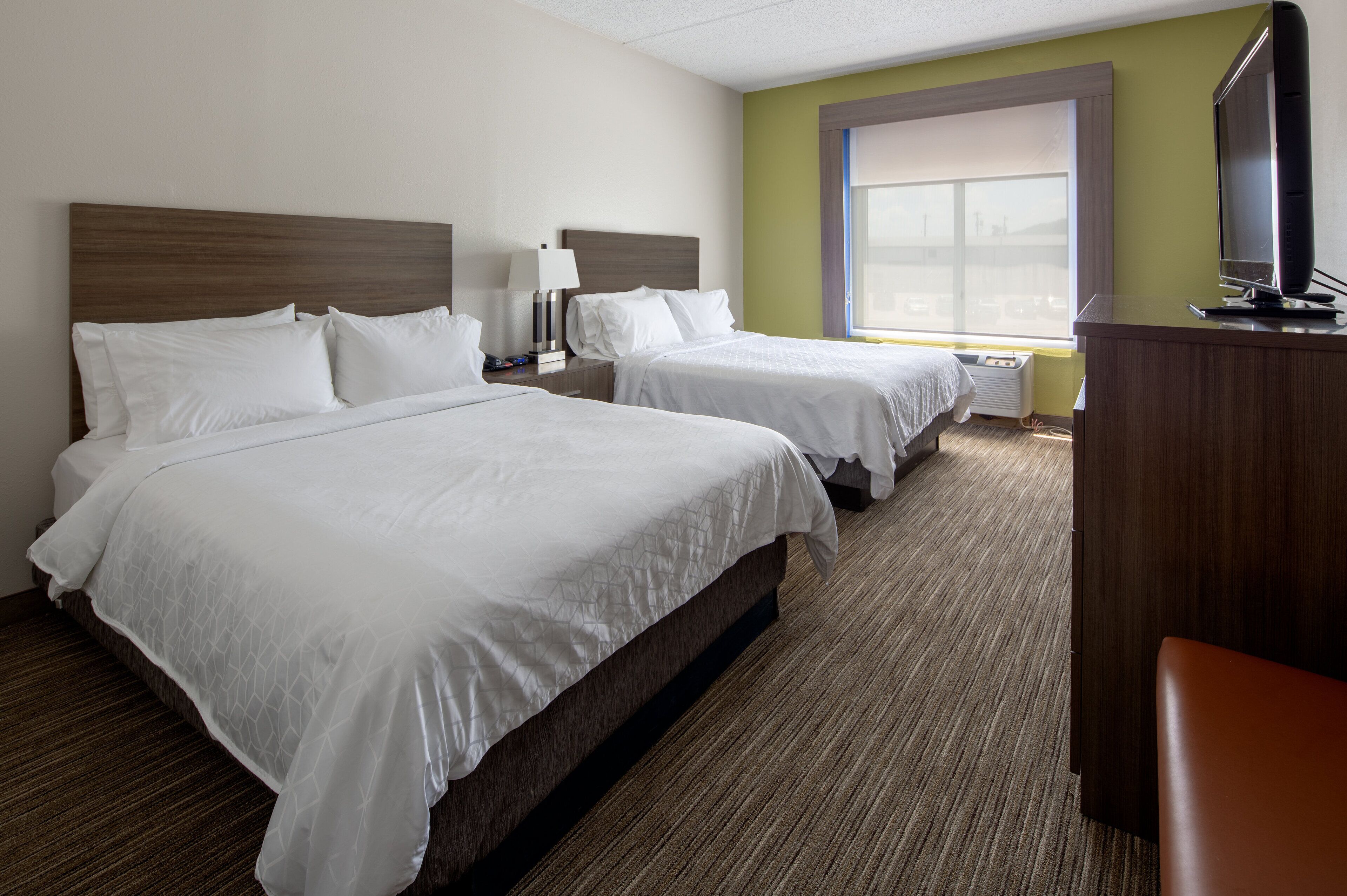 A hotel room with two beds, a desk, a lamp, and a television.
