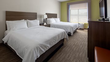A hotel room with two beds, a desk, a lamp, and a television.