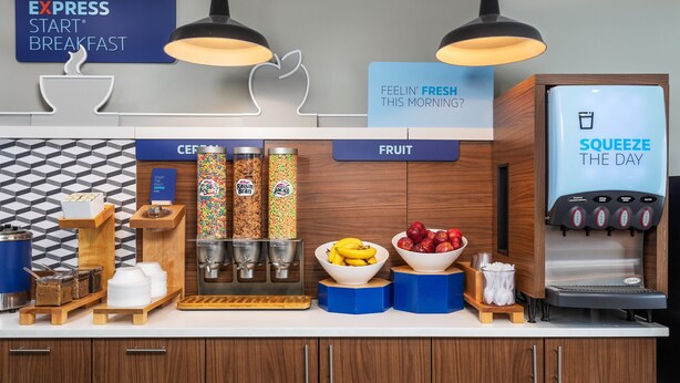 Una barra de desayuno con una máquina de café, cuencos de fruta y dispensadores de cereales.