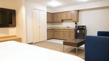 Una habitación de hotel con cama, escritorio, silla, televisión, kitchenette y puerta.