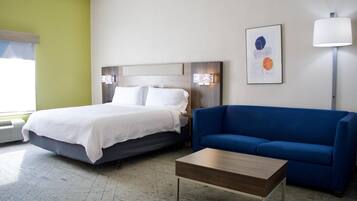 Una habitación de hotel con cama, sofá azul, mesita de madera y lámpara de pared.