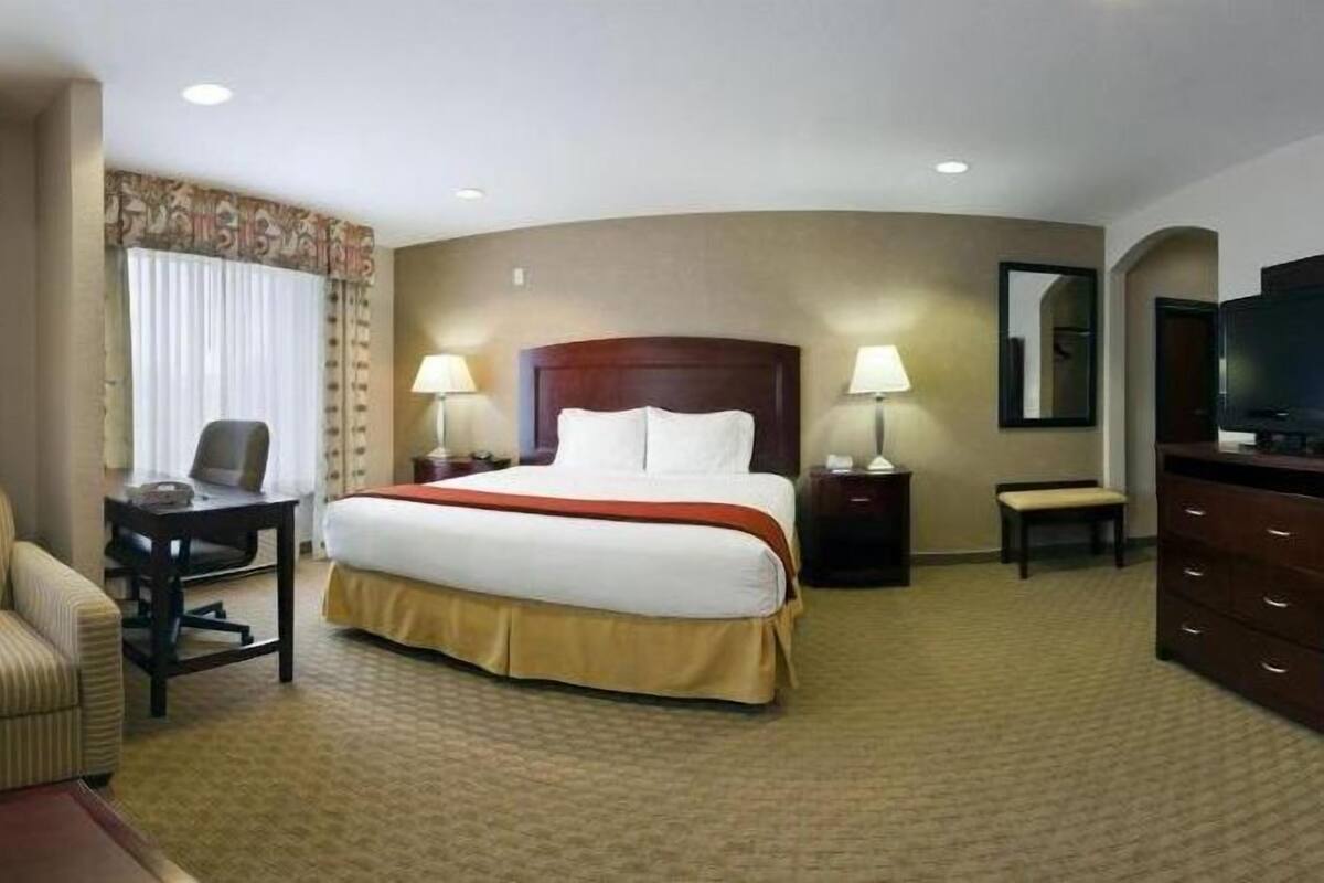 A hotel room with a large bed, a desk with a chair, a television, and a dresser.
