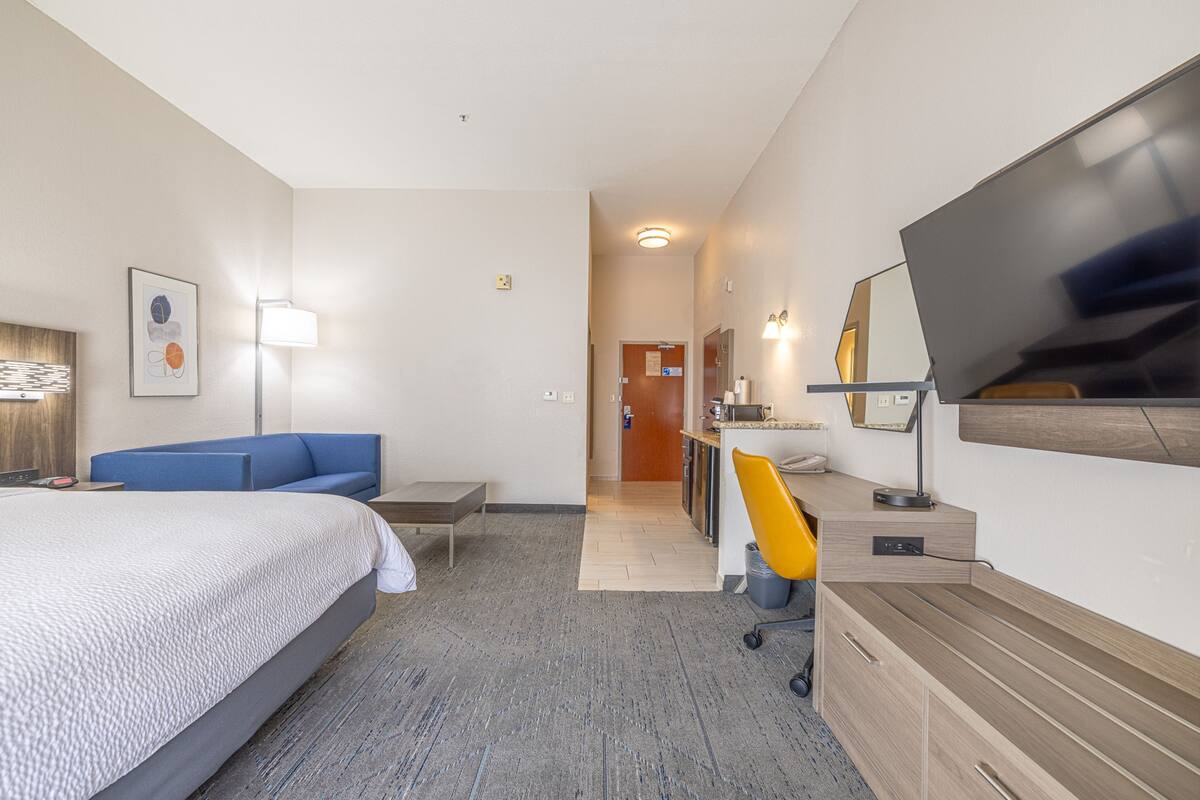 A hotel room with a bed, a desk, a chair, a TV, and a bathroom visible through an open door.