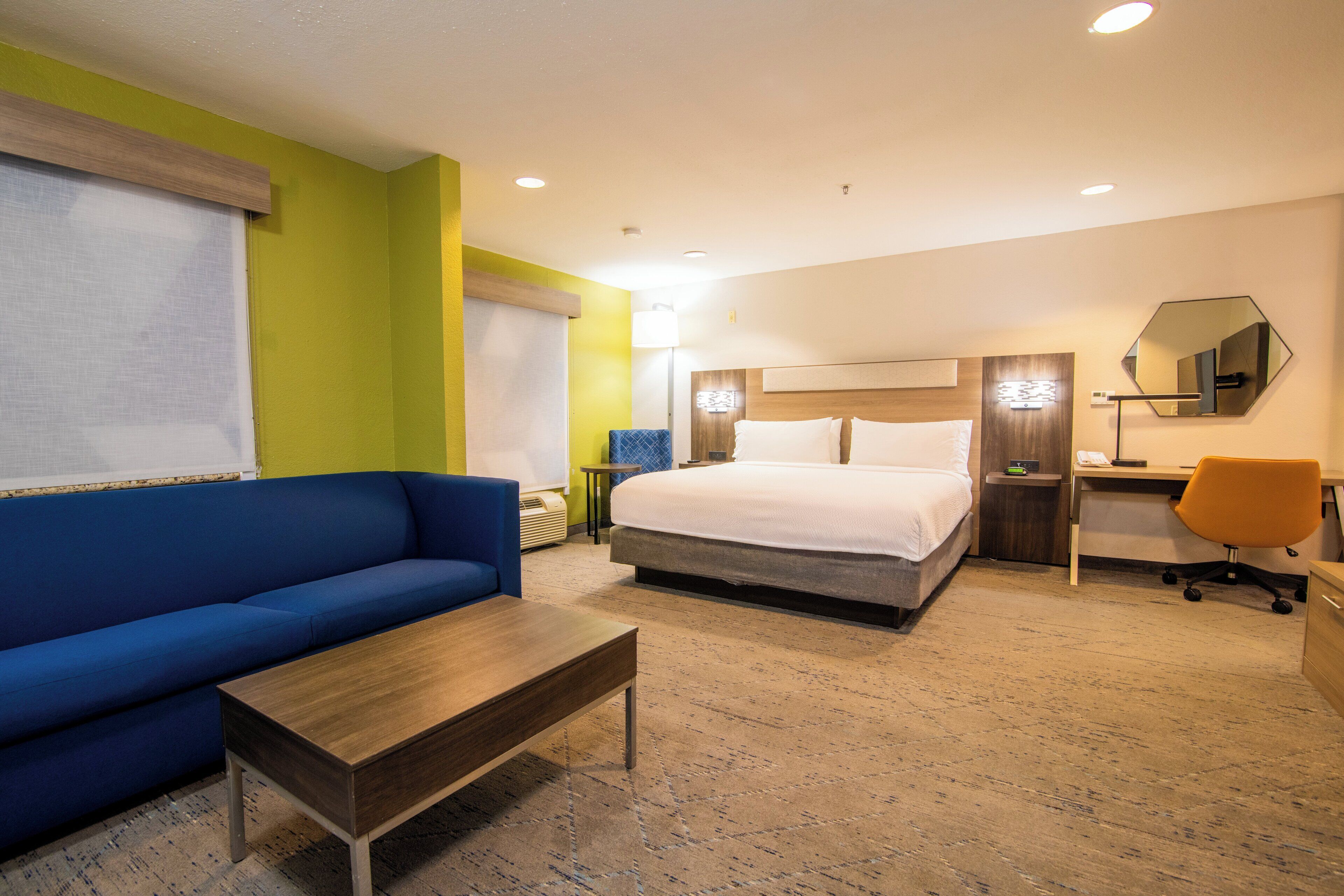 Une chambre d’hôtel avec un lit, un canapé bleu, une table basse en bois, un bureau avec une chaise et un miroir au mur.