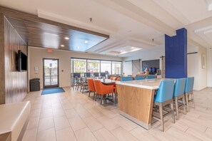 A modern dining area with a central island, orange chairs, and a blue accent wall. - Holiday Inn Express & Suites College Station by IHG (College Station)