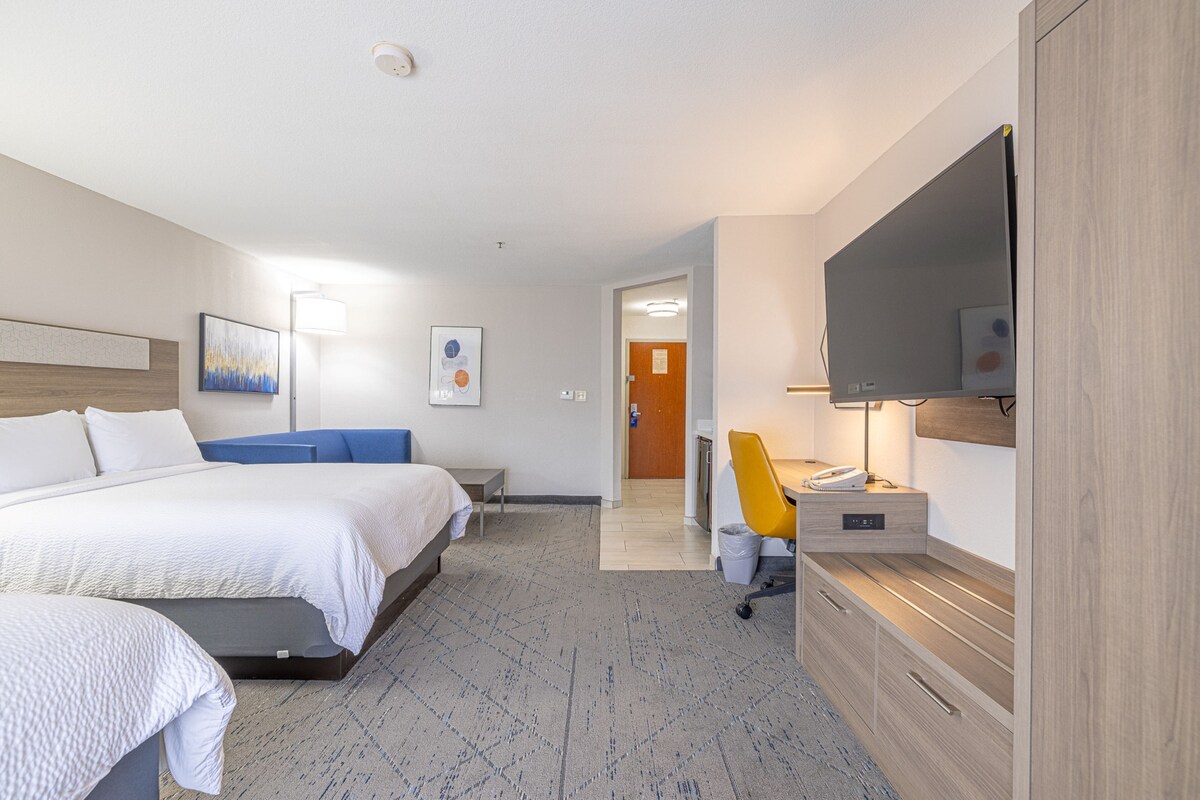 Habitación de hotel con cama, mesita de noche, silla, escritorio, televisión y obras de arte en las paredes.