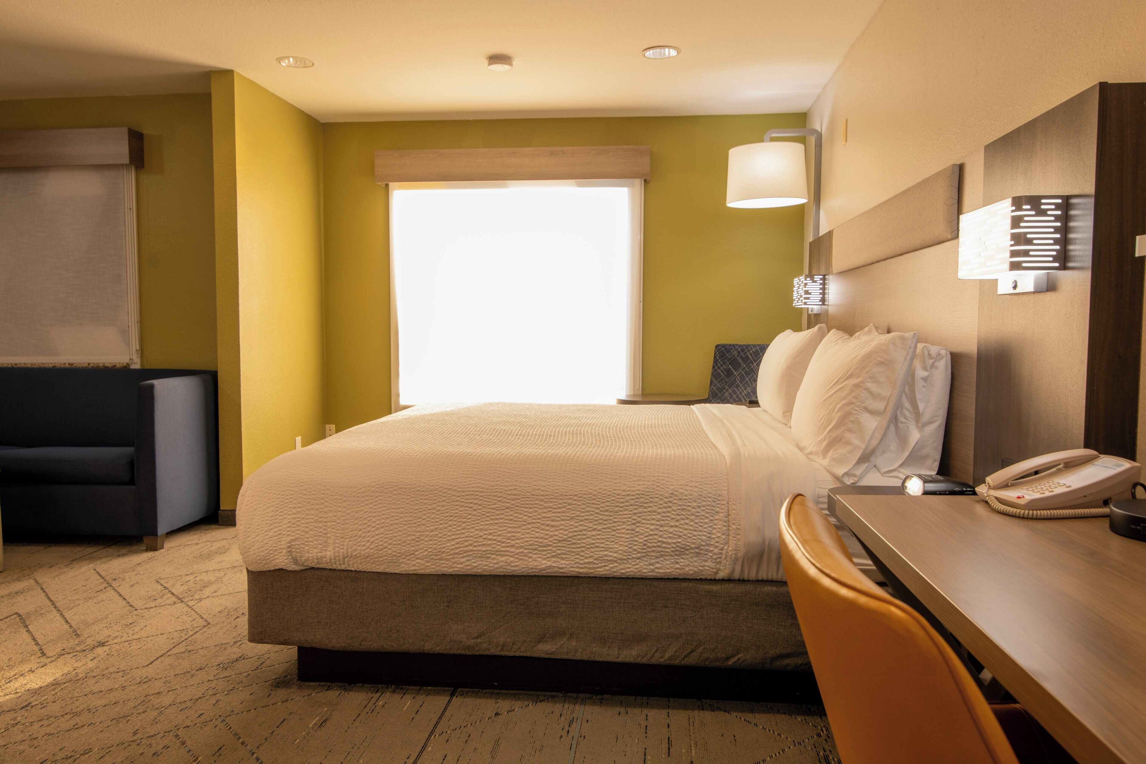 Une chambre d’hôtel avec un lit, un bureau, une chaise, une lampe et un téléphone.